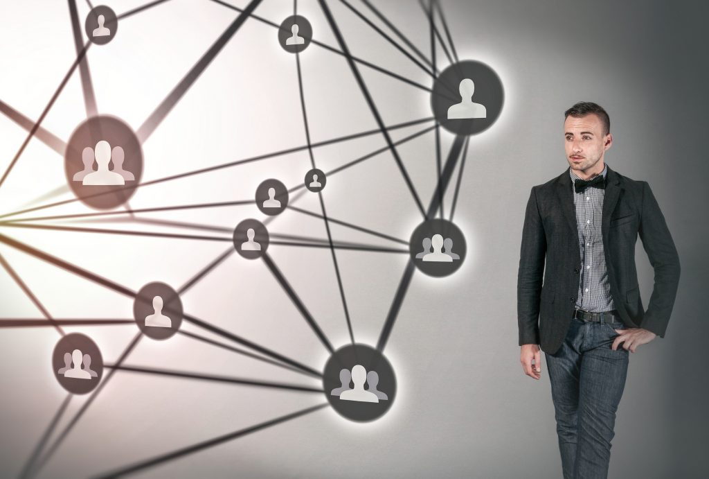 An example of a tacky stock image. A man in a suite stands on the right side of the image. On his left is a web of different people-shaped icons, all connected together with lines.